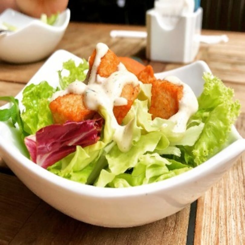Fresh green and red lettuce salad with crispy croutons and creamy dressing in a white bowl.