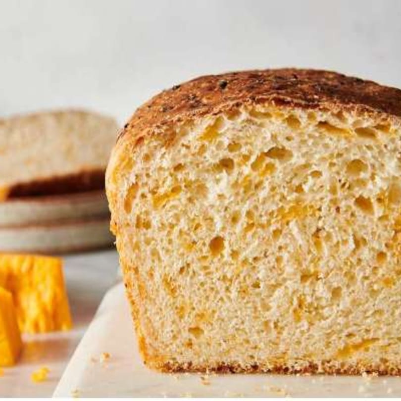 A close-up of a sliced loaf of golden-brown cheese bread with a soft, airy interior.