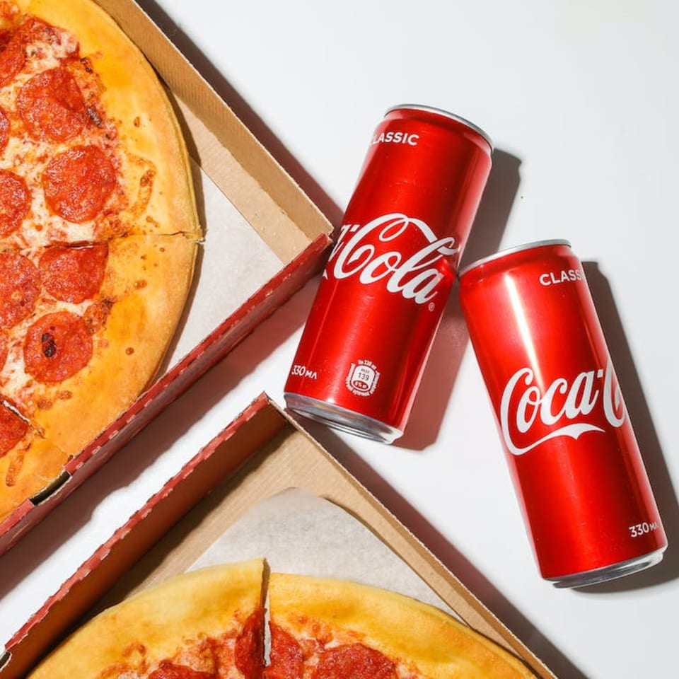 Two Watt A Pizza pepperoni pizzas in boxes with two Coca-Cola cans on a white surface.