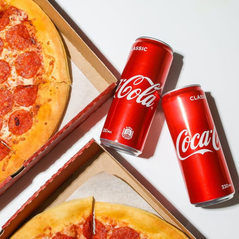 Two Watt A Pizza pepperoni pizzas in boxes with two Coca-Cola cans on a white surface.