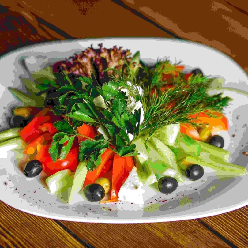 A fresh salad with red tomatoes, green cucumbers, black olives, and herbs on a white plate.